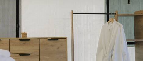 Habitación de hotel con tocador de madera, cama con ropa blanca y bata colgada en un perchero de madera.