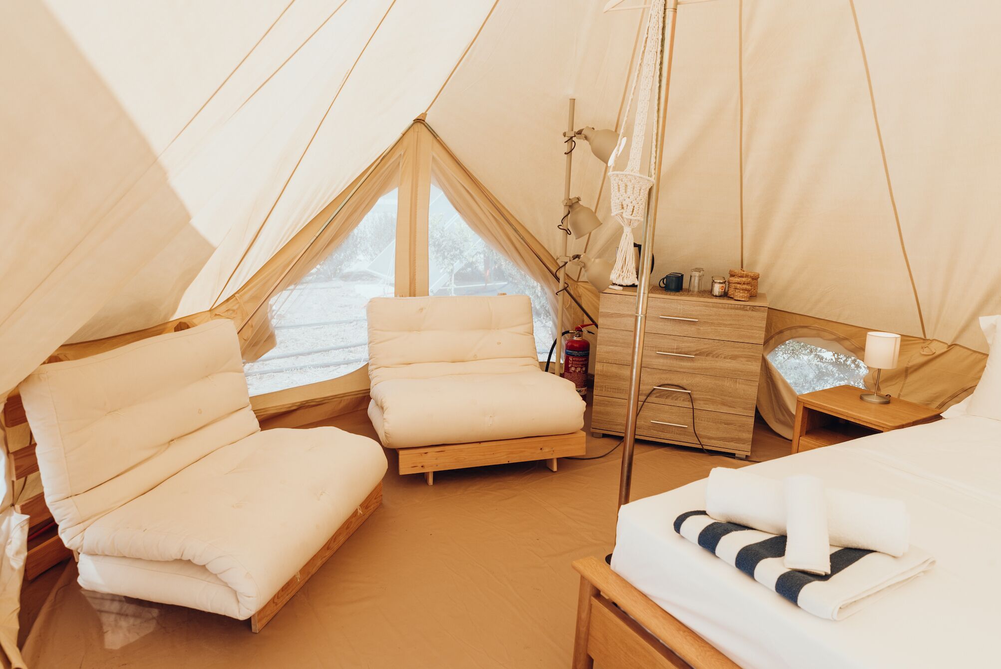 A cozy tented accommodation with a bed, a chair, a small desk, and a bedside table.