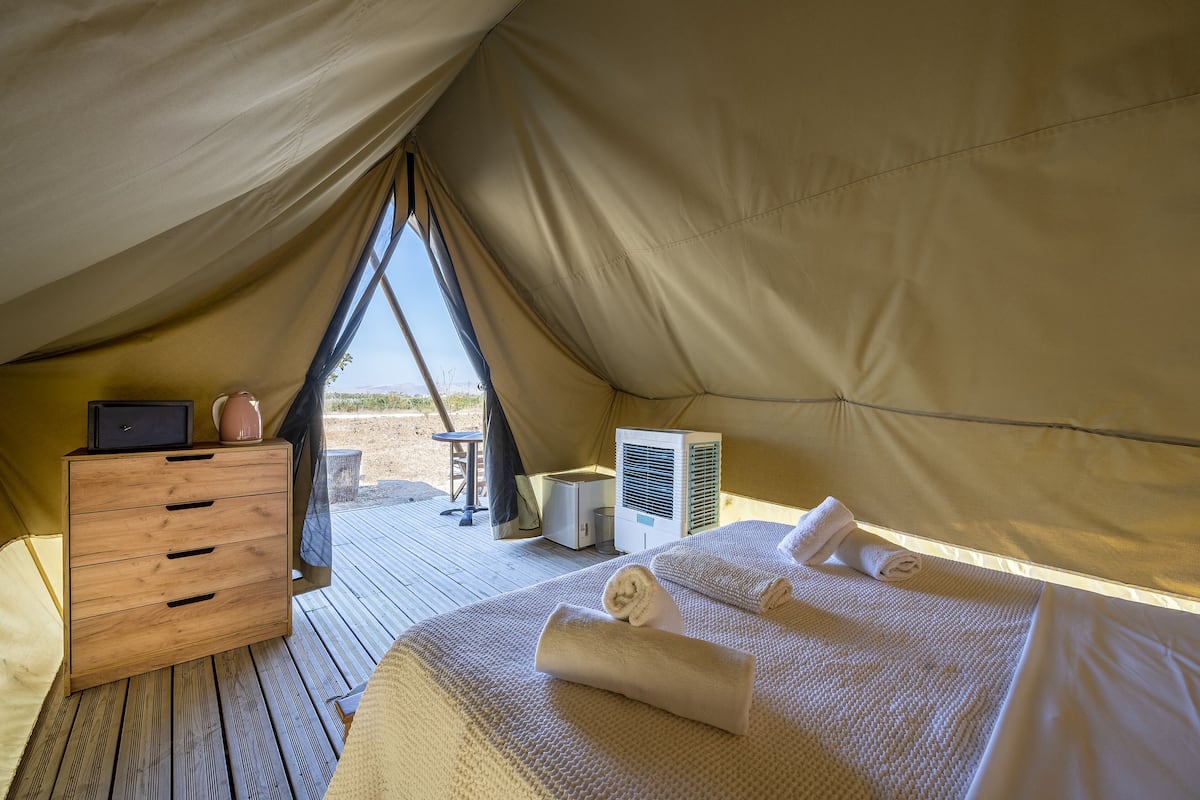 Una carpa con un aparador de madera, una cama con toallas y un equipo de aire acondicionado.