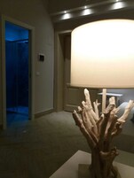 Una stanza con una lampada moderna, una scultura in legno e una porta che dà su uno spazio poco illuminato.