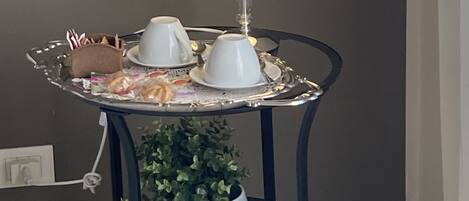 A small round table with a white lamp, a tray with cups and pastries, and a potted plant.