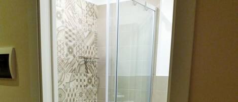 A glass-enclosed shower with patterned tiles and a white towel on the floor.