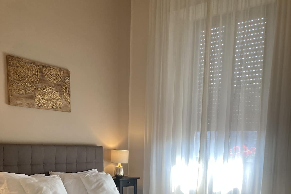 Una cama grande con cabecera gris, ropa de cama blanca y una mesita de noche con lámpara.