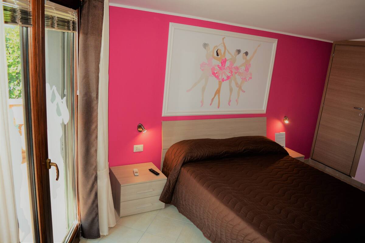 A bedroom with a bed, a nightstand, a lamp, a wardrobe, and a painting on the wall.