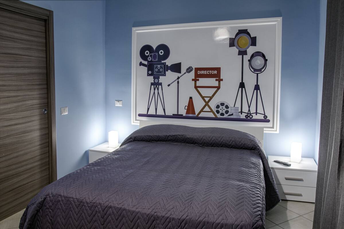 A bedroom with a bed, nightstands, a wall-mounted TV, and a framed picture of film equipment.
