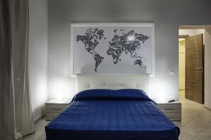 A bedroom with a bed, a nightstand, a drawer, a world map artwork on the wall, and a wooden door. - Artistico Relax B&B (Venticano)