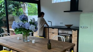 A modern kitchen with a wooden table and yellow chairs, a person washing dishes, and a view of greenery outside. - Casa Lourido (Sada)