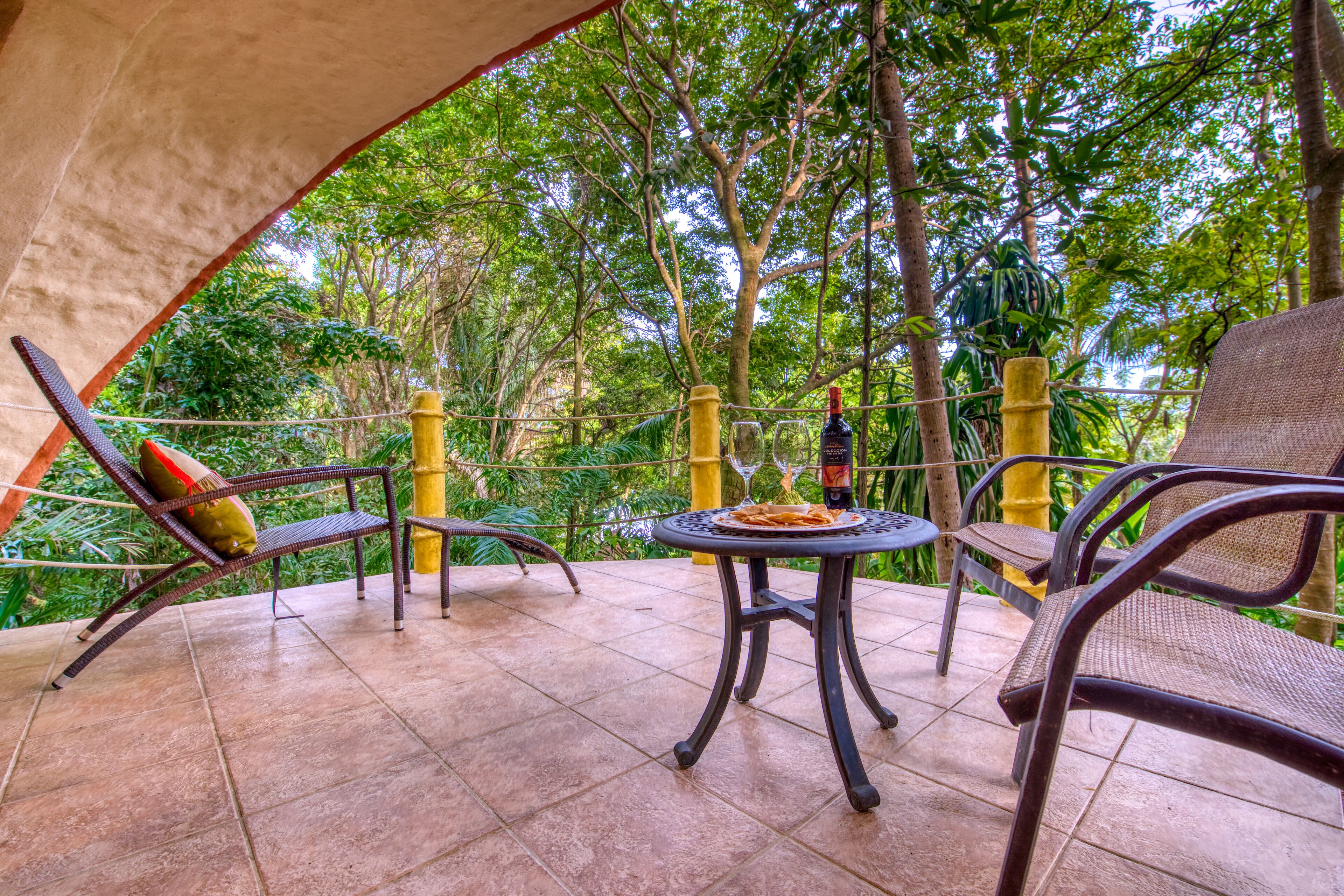 Une terrasse extérieure aménagée avec des meubles en osier, une table ronde et une vue sur une végétation luxuriante.