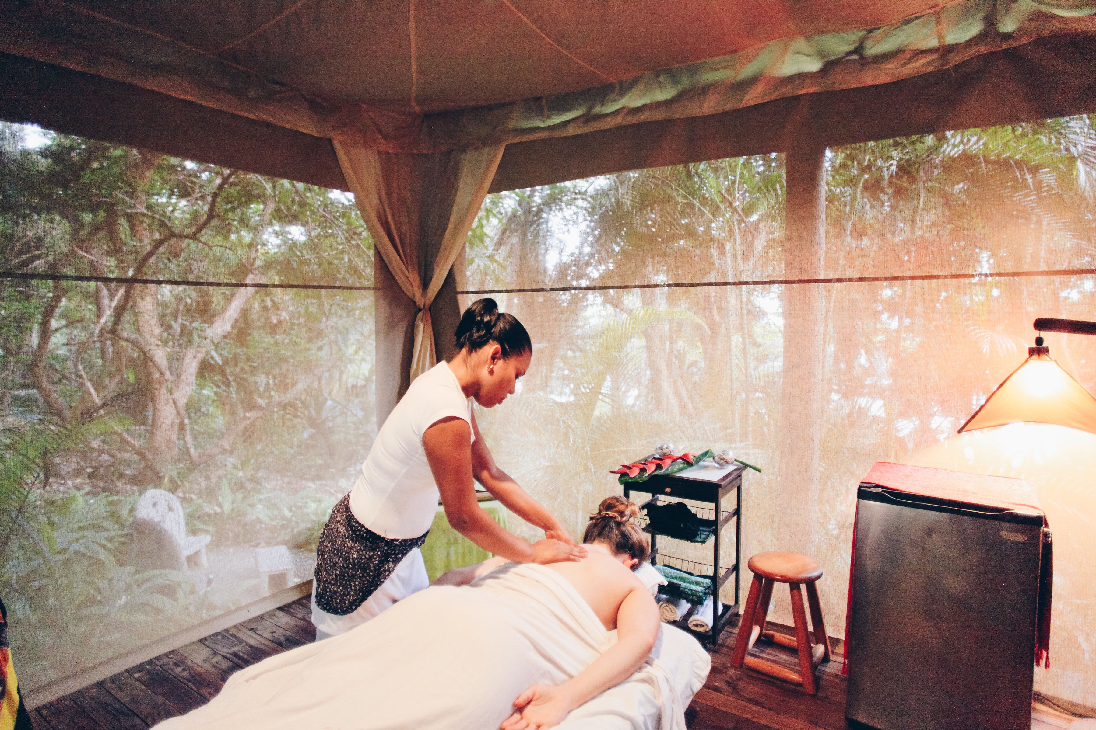Une séance de massage dans un espace aménagé comme une tente, avec vue sur les arbres à travers de fines rideaux.