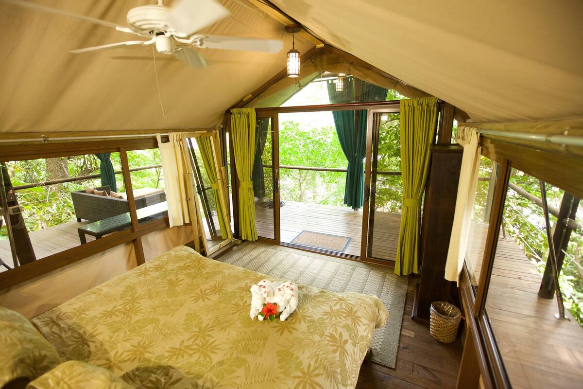 A tented accommodation with a bed, a ceiling fan, and a view of the outdoors.