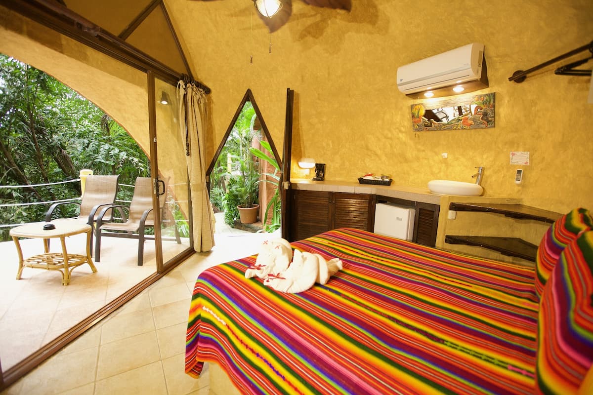 A room with a bed, a bathroom, and a balcony with chairs and a table.