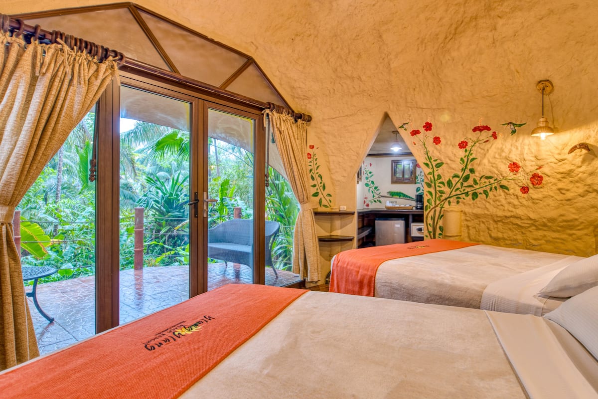 A room with two beds, a sliding glass door to a garden, and a wall with floral decorations.