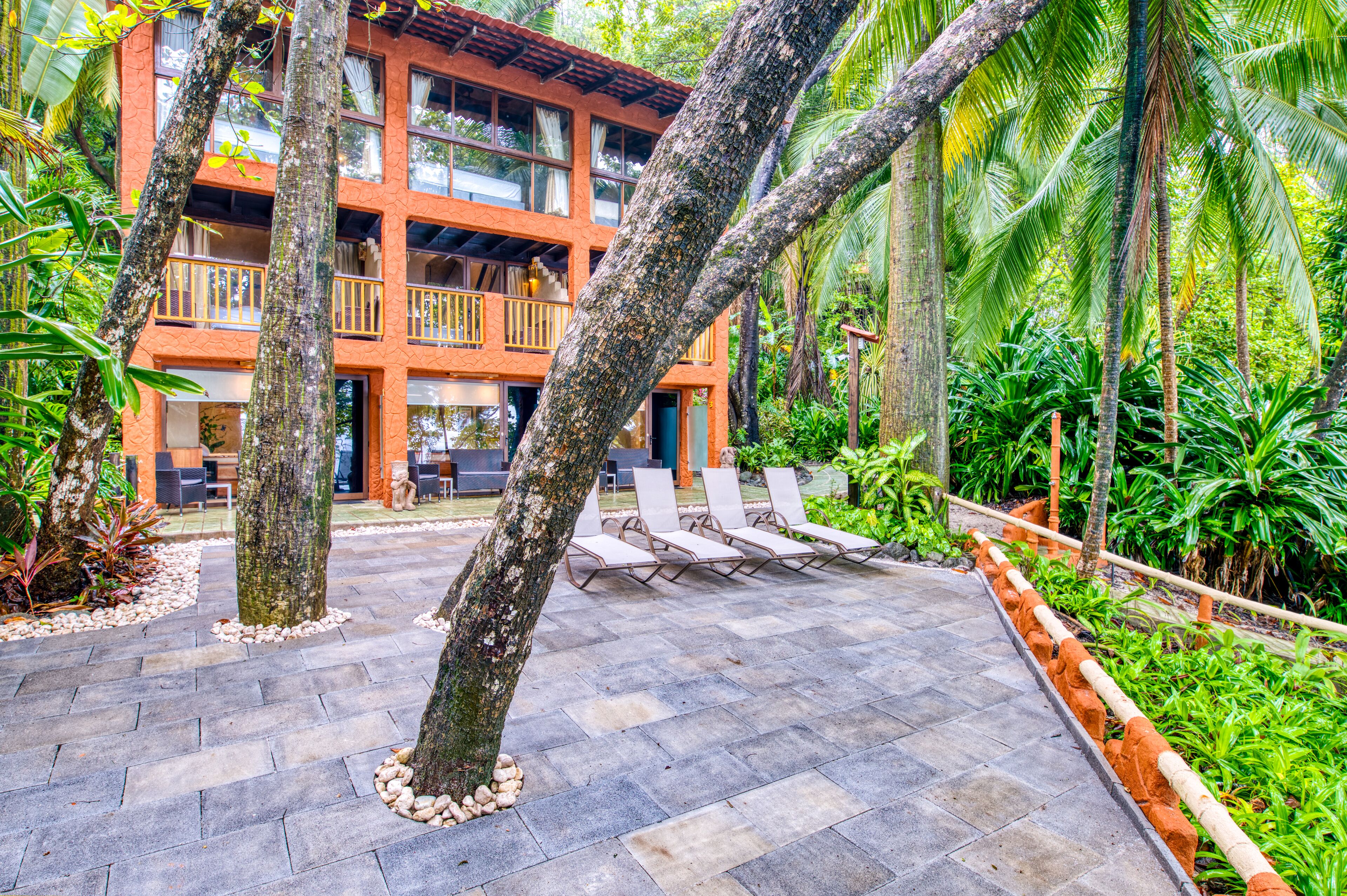 A multi-story building with a balcony, surrounded by lush greenery and palm trees.