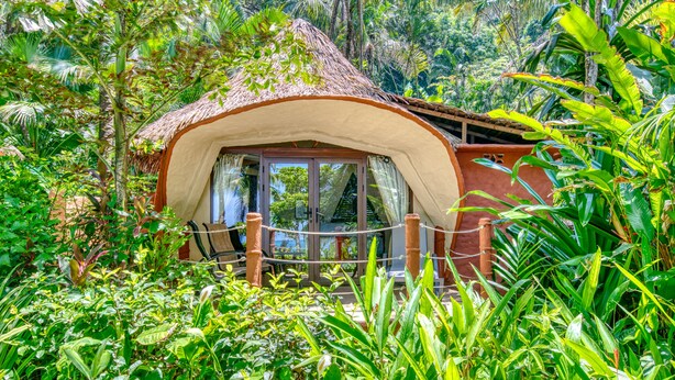 Una construcción con techo de paja rodeada de abundante follaje tropical.