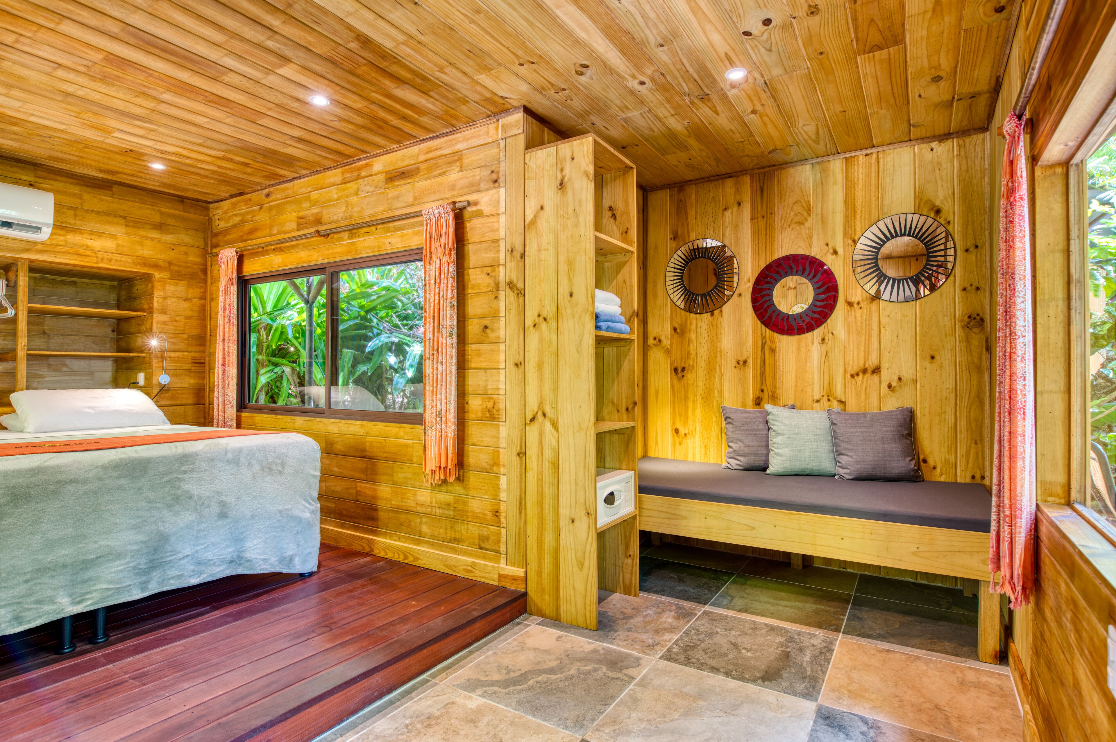 Una habitación de cabaña de madera con una cama, un banco y una ventana con cortinas.