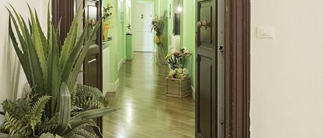 Un pasillo con una puerta verde, un felpudo con el texto 'RESIDENCY' y una planta a la izquierda.