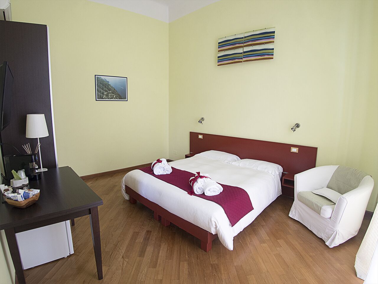 A hotel room with a bed, a chair, a desk, and a lamp.