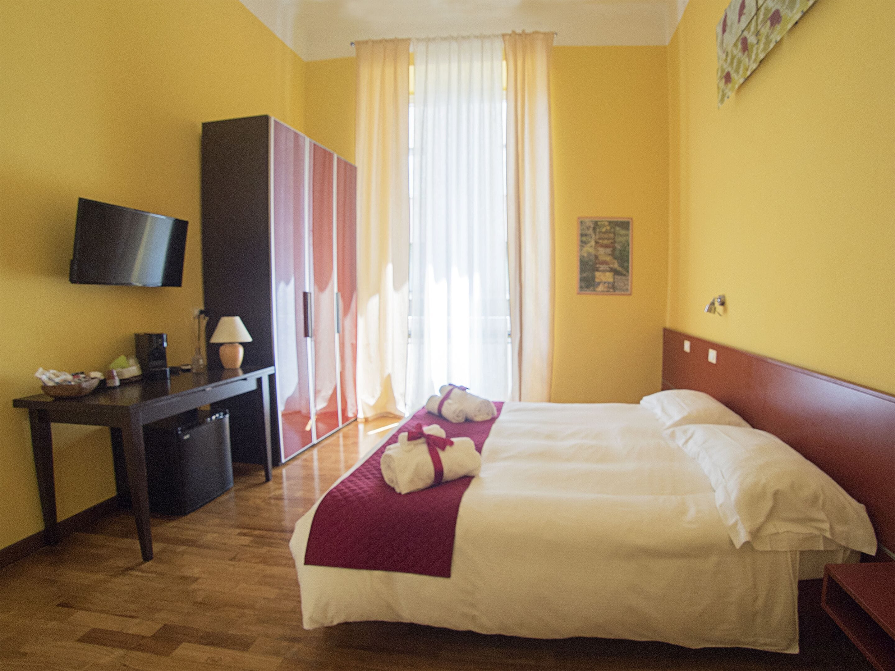 A hotel room with a bed, a desk, a television, and a window with curtains.