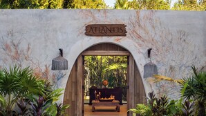 Una entrada arqueada con la leyenda "Atlantis", un sendero de piedra que conduce a un banco de madera y una mesa con un cuenco decorativo.