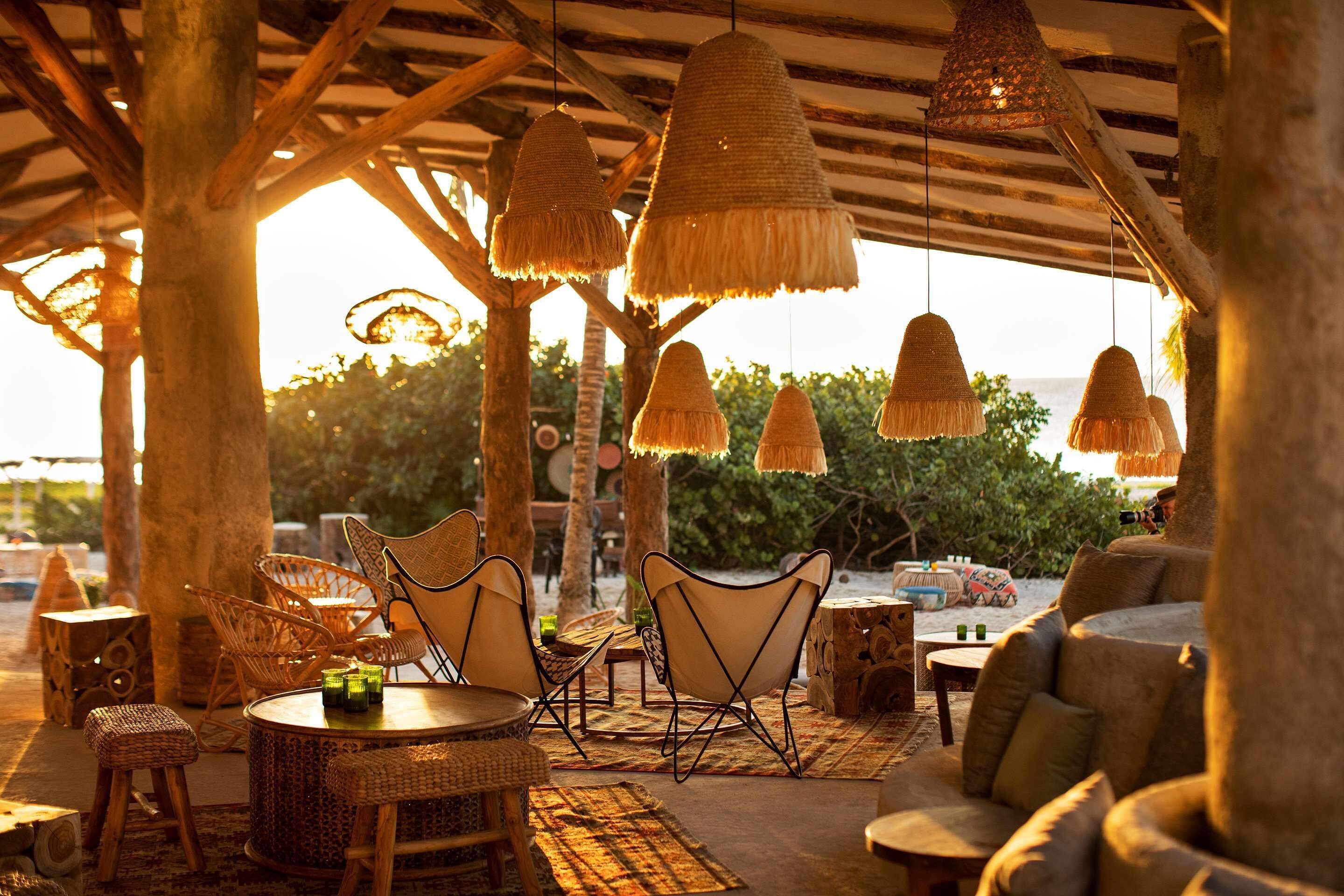 Un espacio al aire libre con mobiliario de mimbre y lámparas colgantes, con vistas a un paisaje natural.