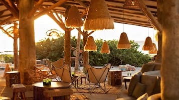Un espacio al aire libre con mobiliario de mimbre y lámparas colgantes, con vistas a un paisaje natural.
