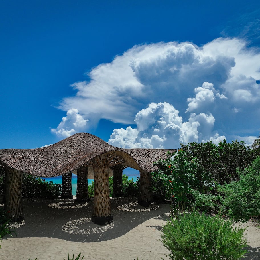 A beachside structure with a thatched roof, surrounded by greenery and a clear blue sky.