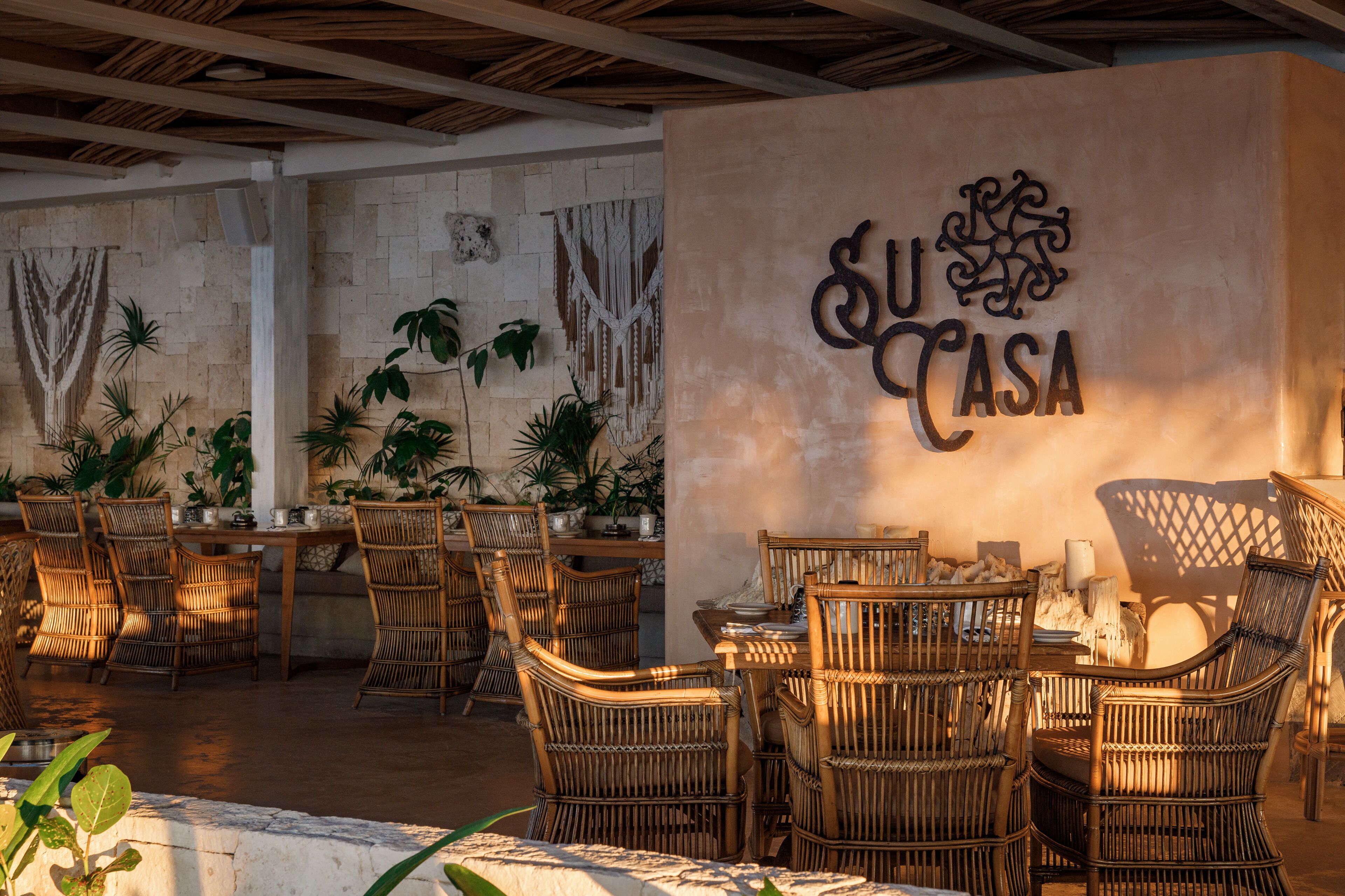 An outdoor dining area with wicker furniture and a wall with 'SU CASA' signage.