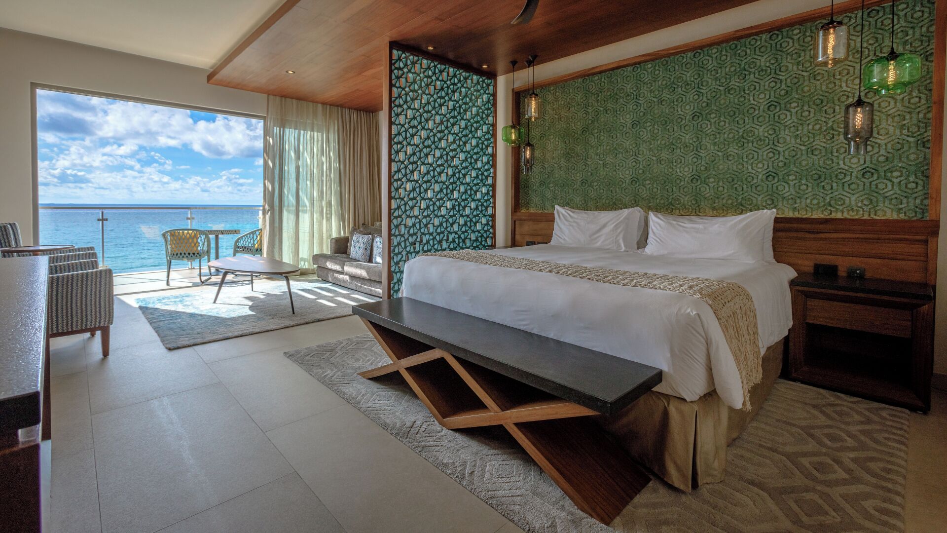 A hotel room with a bed, a desk, a chair, a view of the sea, and a patterned wall.