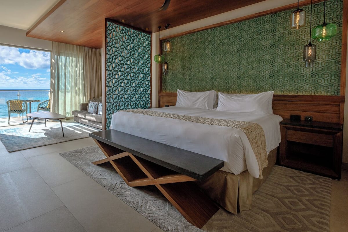 A hotel room with a bed, a desk, a chair, a view of the sea, and a patterned wall.