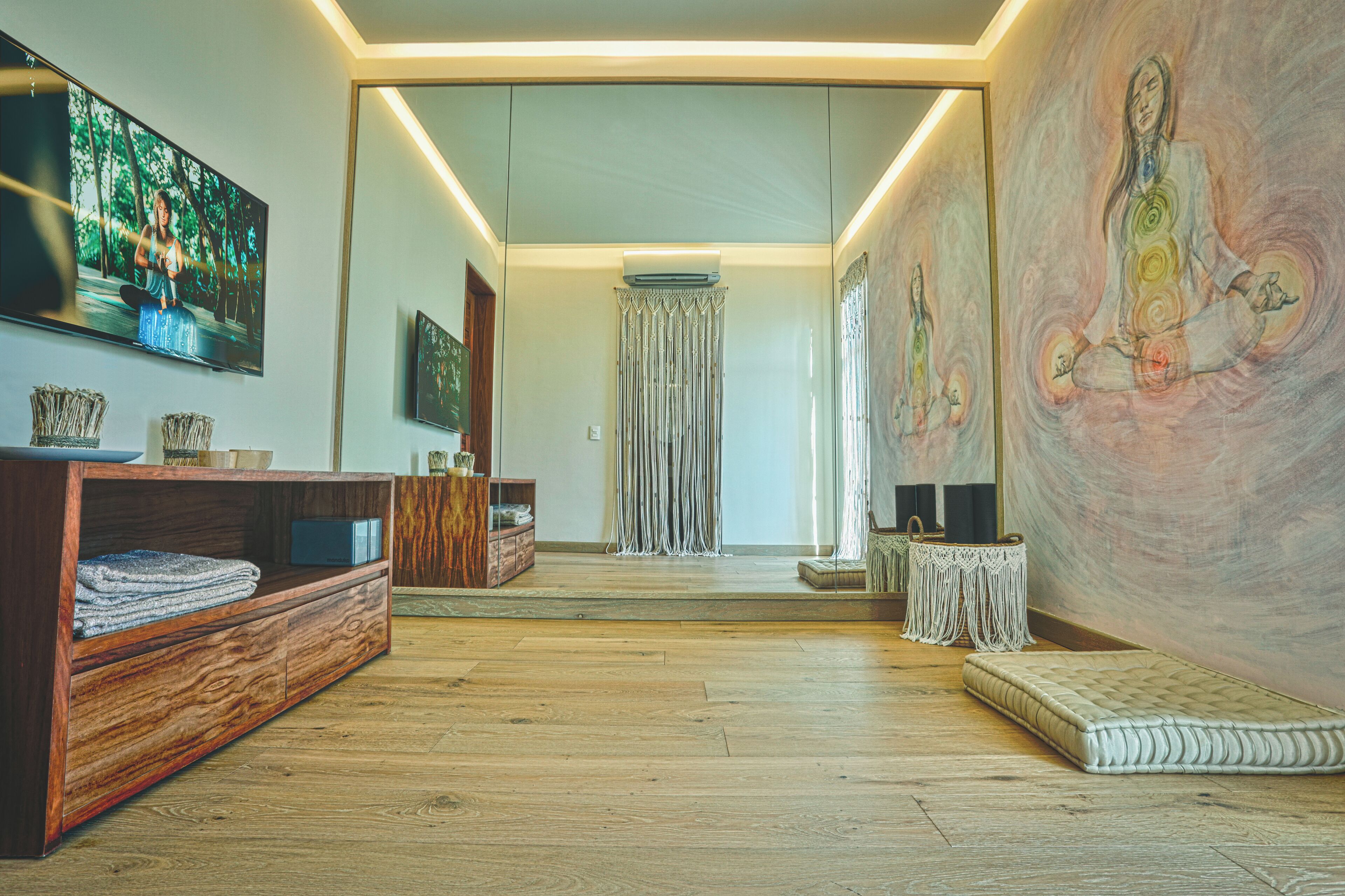 A spacious room with a wooden floor, a large painting on the wall, and a television mounted on the wall.