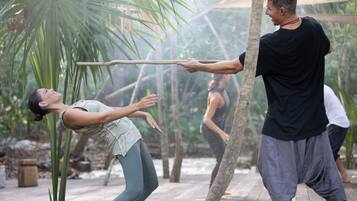 A person performing a physical activity outdoors, possibly a martial arts or yoga pose, with a wooden deck and palm trees in the background.