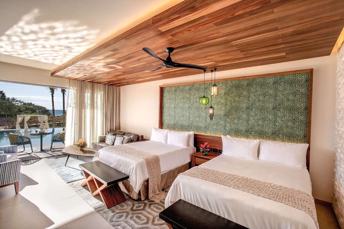 Habitación de hotel con dos camas, un balcón con piscina y vista al océano.
