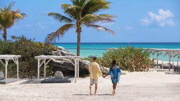 Una pareja caminando sobre una playa arenosa con cielo azul despejado y mar turquesa.