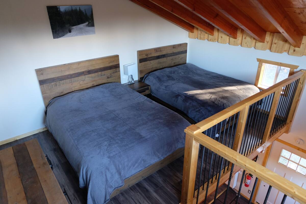 Ein Schlafzimmer mit zwei Betten, Holz-Kopfteilen, einem Nachttisch, einer Lampe und einem gerahmten Bild an der Wand.