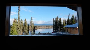 Näkymä mökin ikkunasta, taustalla järvi ja metsä.