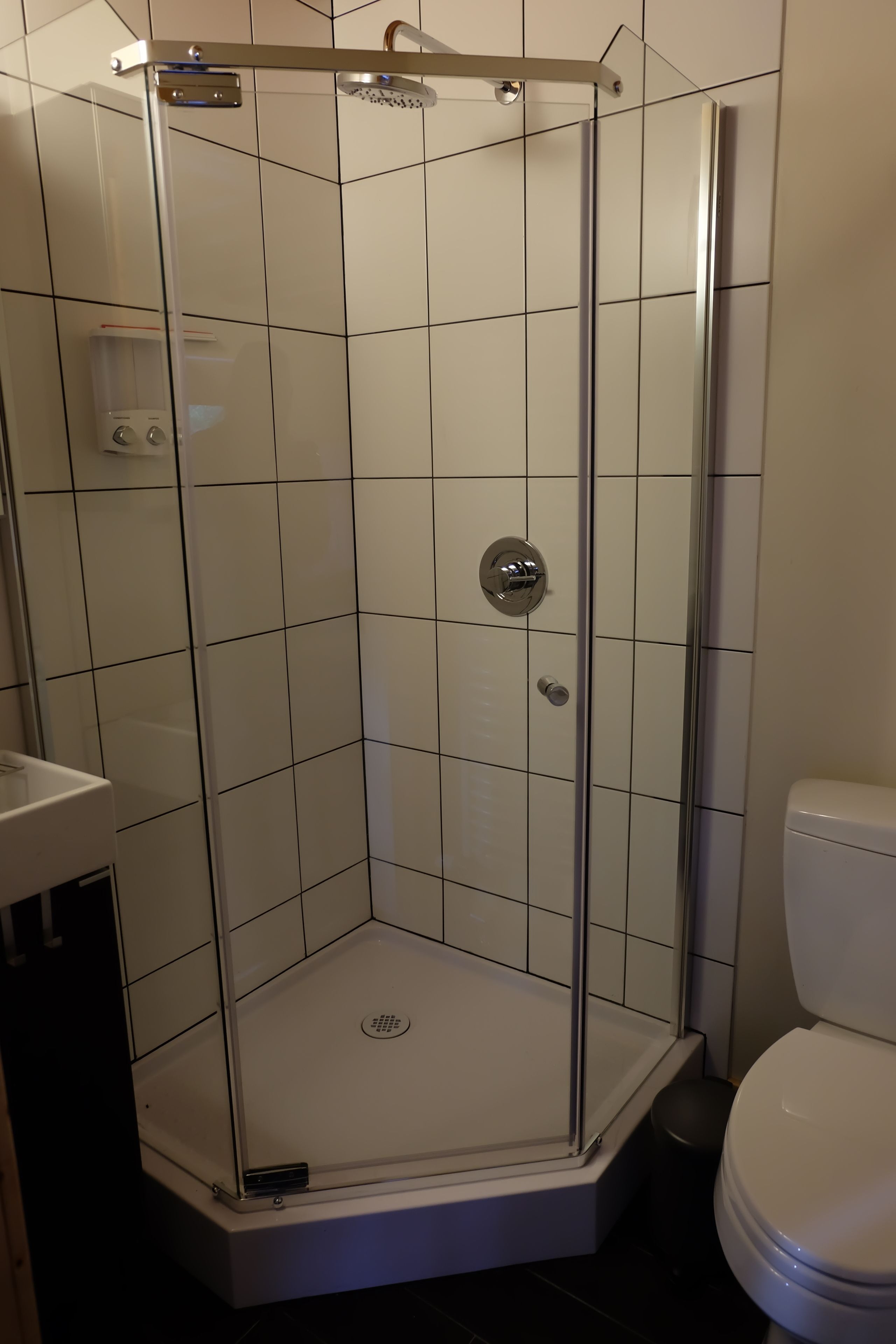 A modern bathroom with a glass-enclosed shower, white tiled walls, and a white toilet.