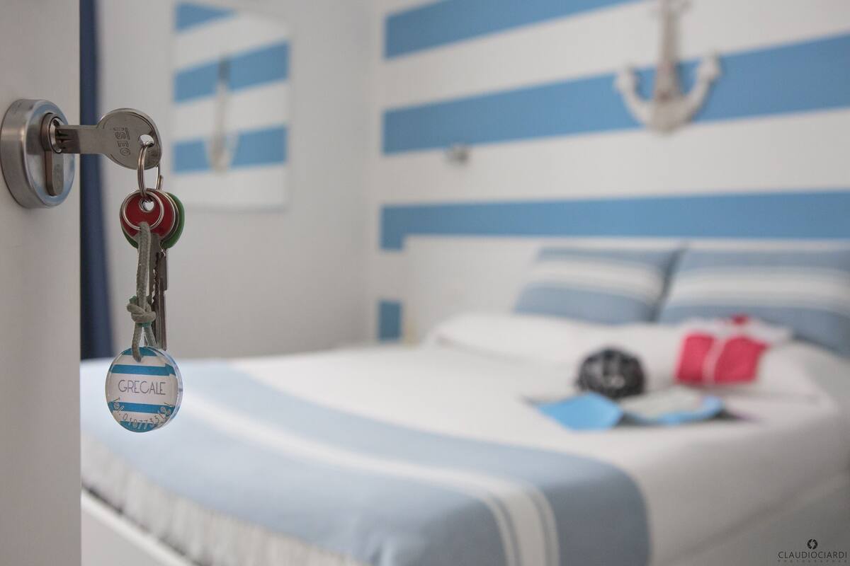 A hotel room with a bed featuring blue and white striped bedding, a keychain with a name tag, and a wall-mounted anchor decoration.