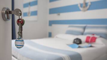 A hotel room with a bed featuring blue and white striped bedding, a keychain with a name tag, and a wall-mounted anchor decoration.