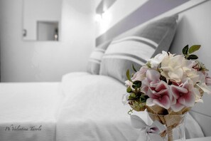 Un lit avec une literie blanche et un bouquet de fleurs dans un vase en verre.
