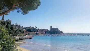 A coastal town with a sandy beach, clear blue waters, and a prominent castle-like structure in the background.