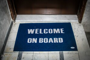 Un paillasson bleu sur lequel on peut lire en lettres blanches : « BIENVENUE À BORD ».