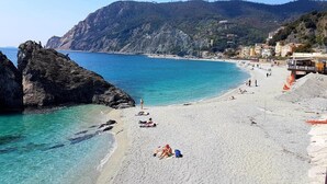 A beach with clear turquoise water, rocky outcrops, and buildings along the coastline. - L'Approdo Dell' Ammiraglio (La Spezia)