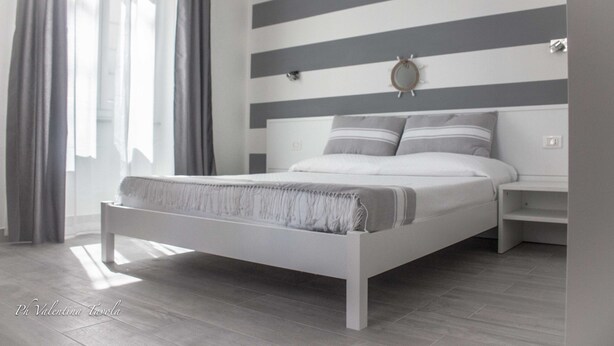 A modern bedroom with a bed, nightstands, and a striped wall. - L'Approdo Dell' Ammiraglio (La Spezia)
