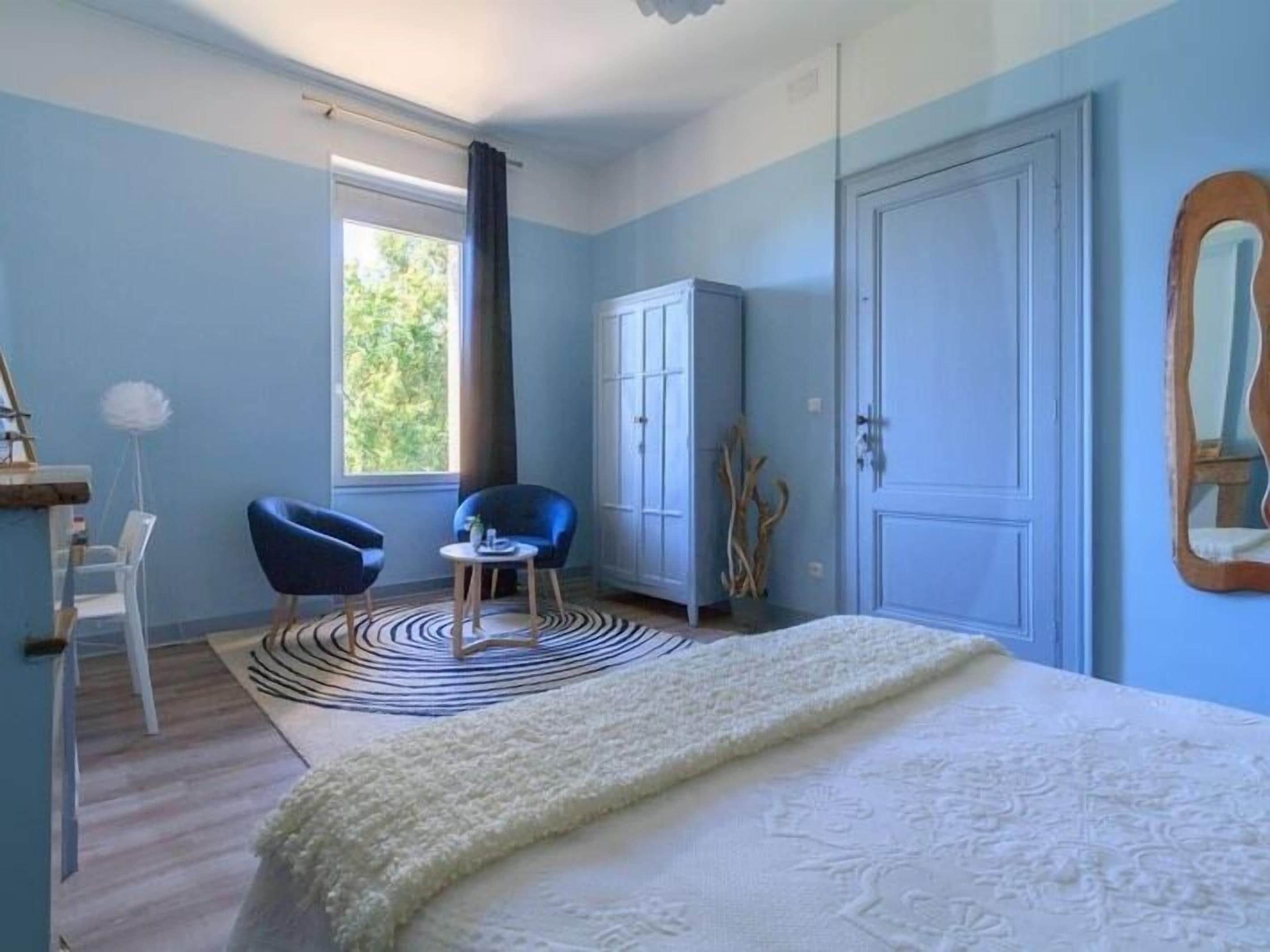 A bedroom with a bed, two chairs, a wardrobe, and a window with curtains.