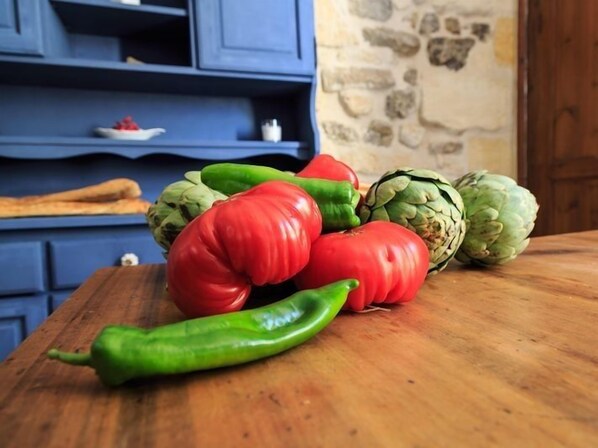 A wooden cutting board with red and green bell peppers, artichokes, and a green chili pepper.