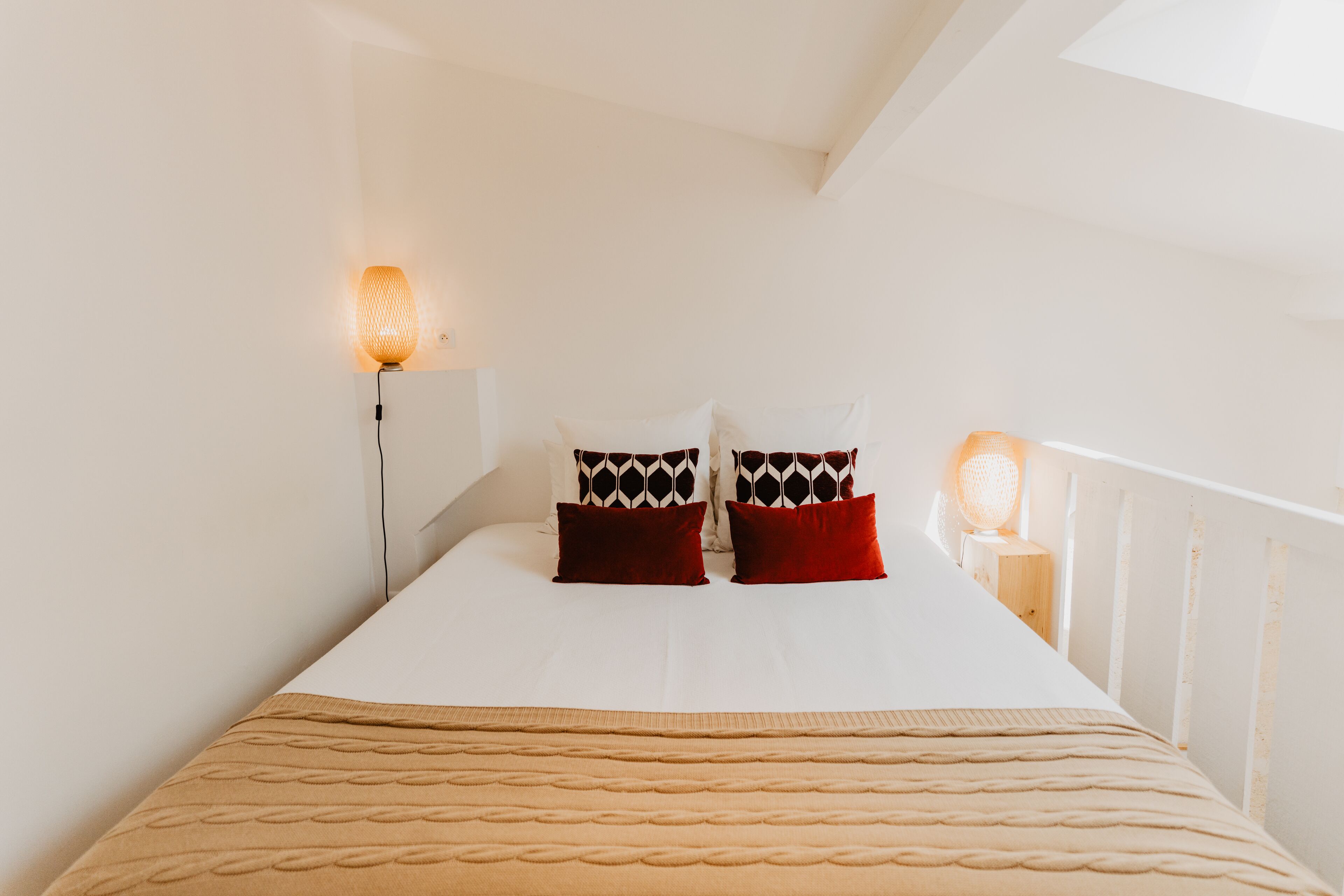 Ein ordentlich bezogenes Bett mit gemusterten Kissen, einer beigen Decke und zwei Nachttischlampen.