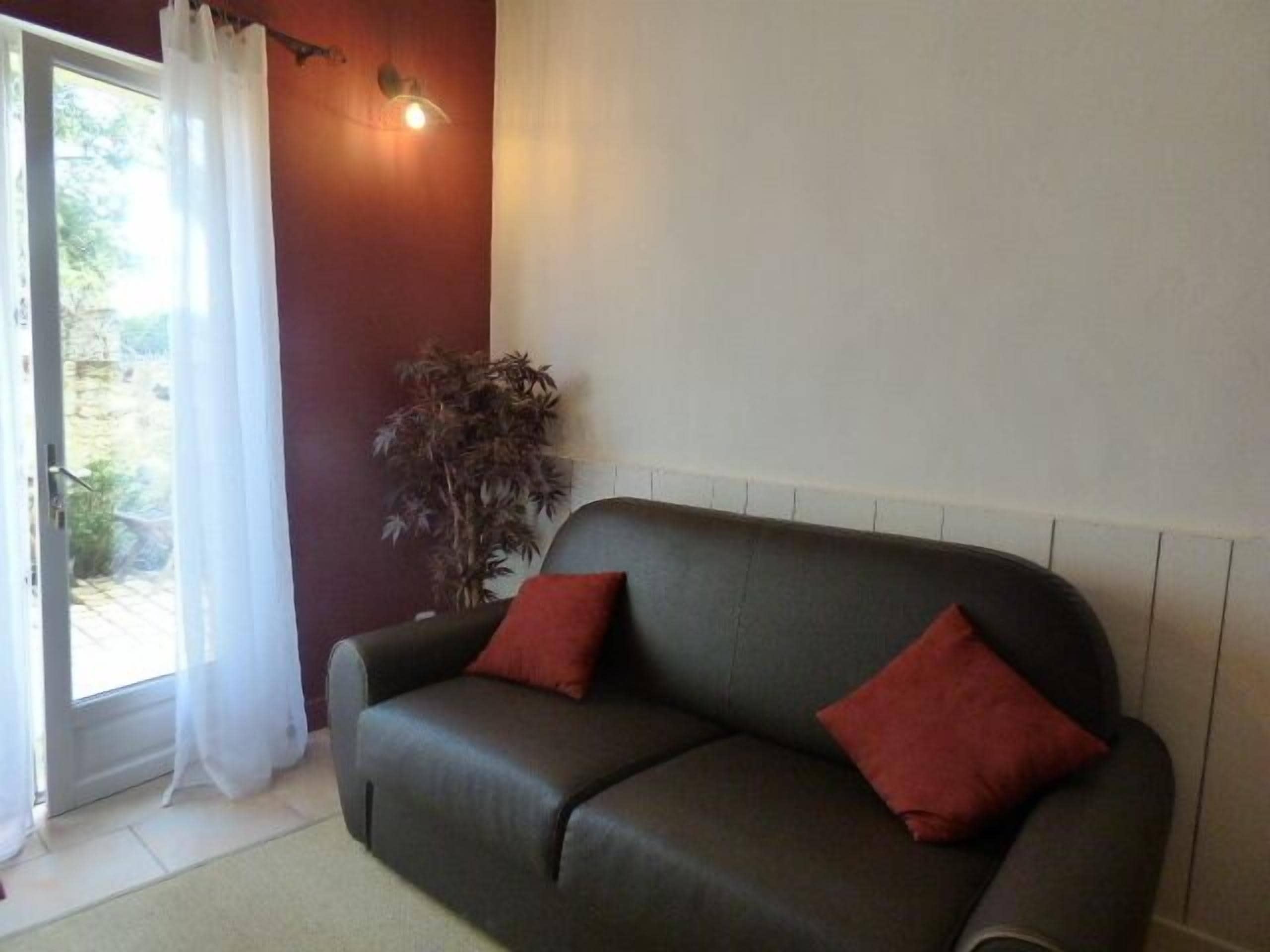 A dark-colored sofa with two red cushions, a potted plant, and a wall-mounted light fixture.