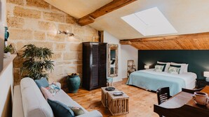 A cozy loft bedroom with a sloped ceiling, a large window, a bed with a blue bedspread, a wooden coffee table, and a sofa. - Le Coeur des Vignes (Pauillac)