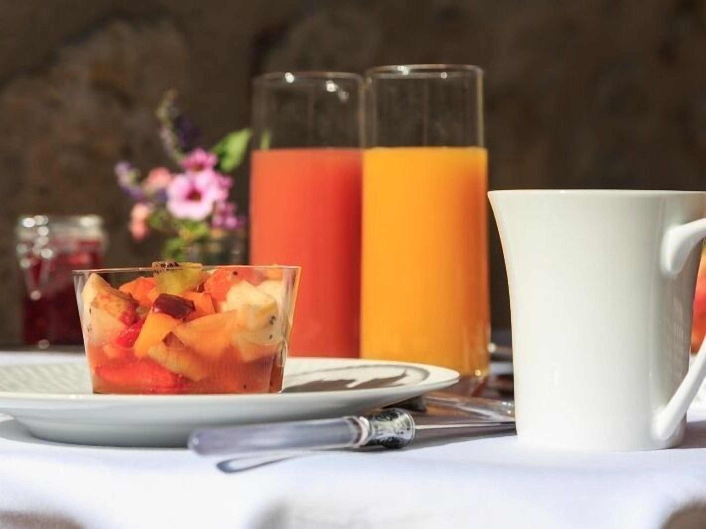 A breakfast setting with a fruit salad, a glass of orange juice, and a white mug on a table.