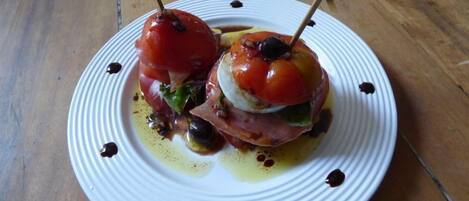 A plate with two stuffed tomatoes on skewers, olive oil, and balsamic glaze on a wooden table.